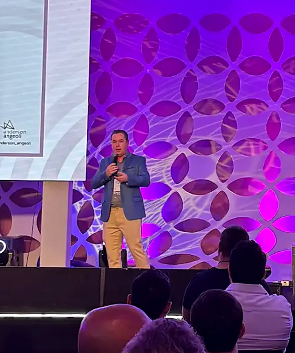 Anderson Angeoli apresentando ao vivo para uma plateia cheia, com as telas do Superbriefing ao fundo